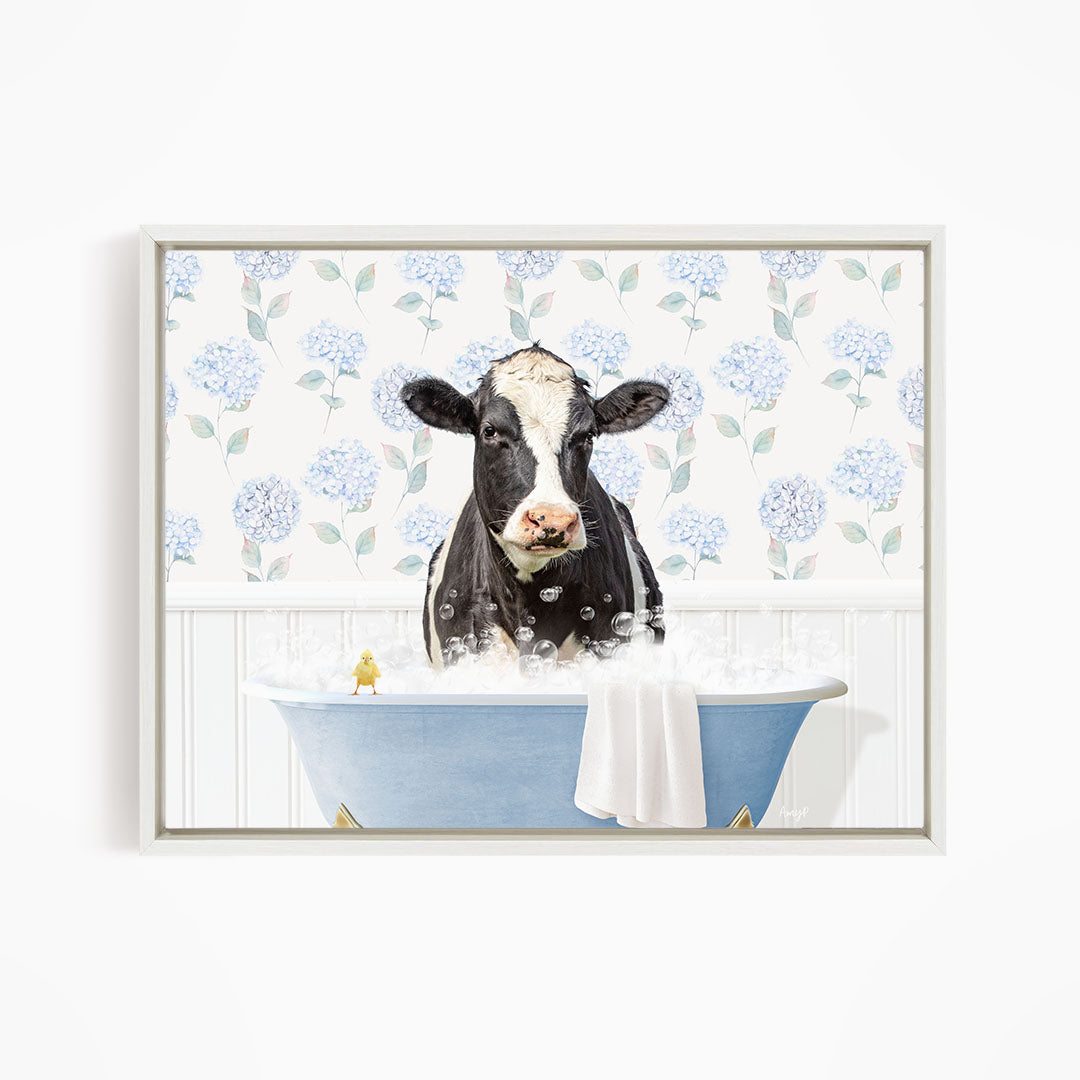 A black and white cow is sitting in a blue bathtub filled with bubbles, with a yellow bird perched on the edge of the tub.