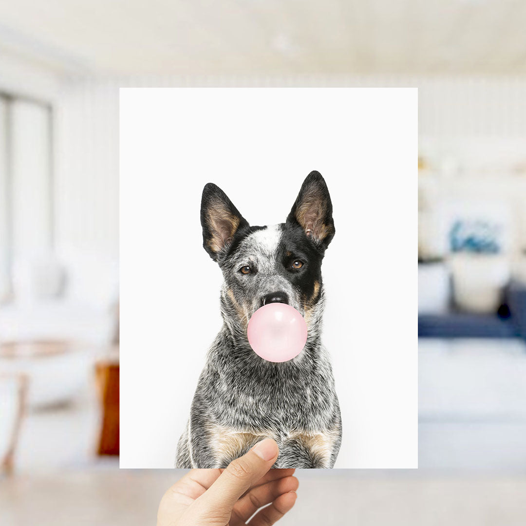 A black and white dog is blowing a bubble with a pink bubble gum bubble in the image.