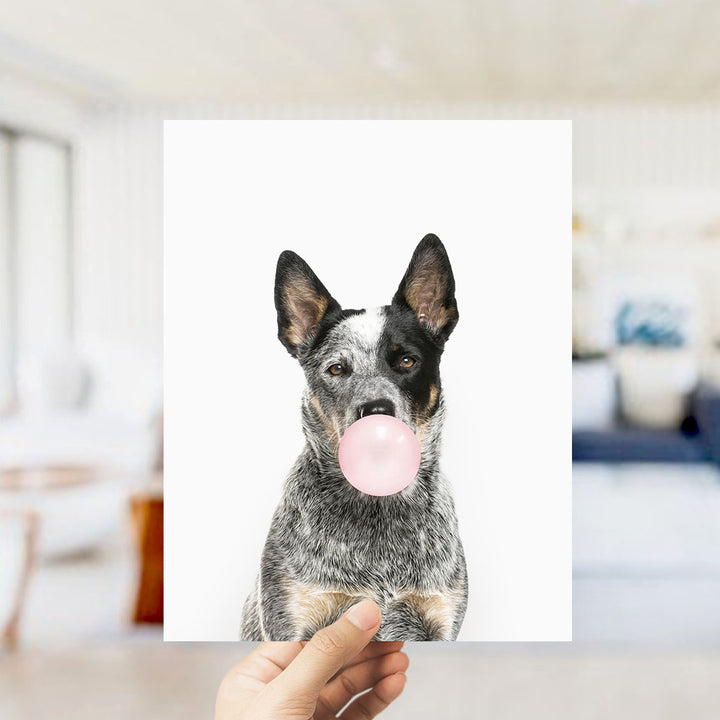 A black and white dog is blowing a bubble with a pink bubble gum bubble in the image.