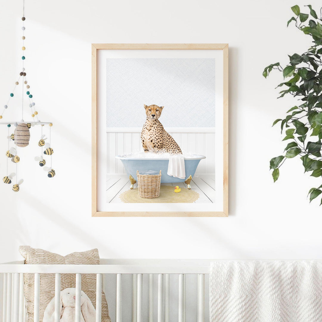 A cheetah sits in a blue bathtub, surrounded by a basket of bath toys and a hanging mobile, in a nursery setting with a white crib and a plant in the background.