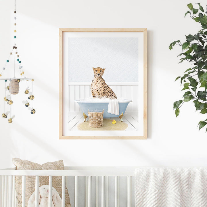 A cheetah sits in a blue bathtub, surrounded by a basket of bath toys and a hanging mobile, in a nursery setting with a white crib and a plant in the background.