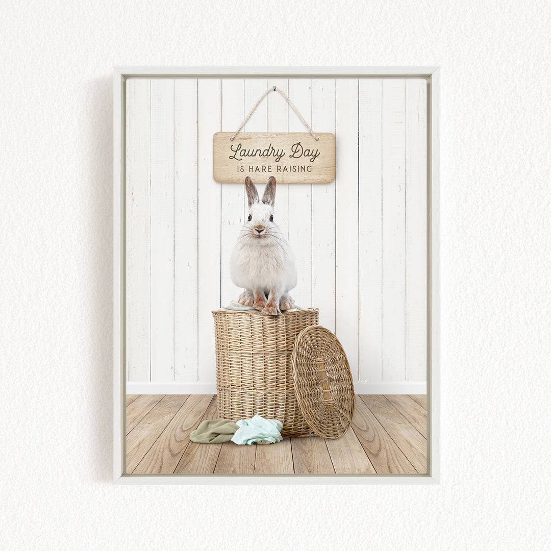 A white rabbit sits atop a wicker basket, with a wooden sign above that reads "Laundry Day is harder raising".