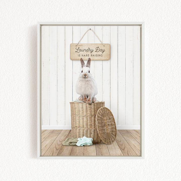 A white rabbit sits atop a wicker basket, with a wooden sign above that reads "Laundry Day is harder raising".