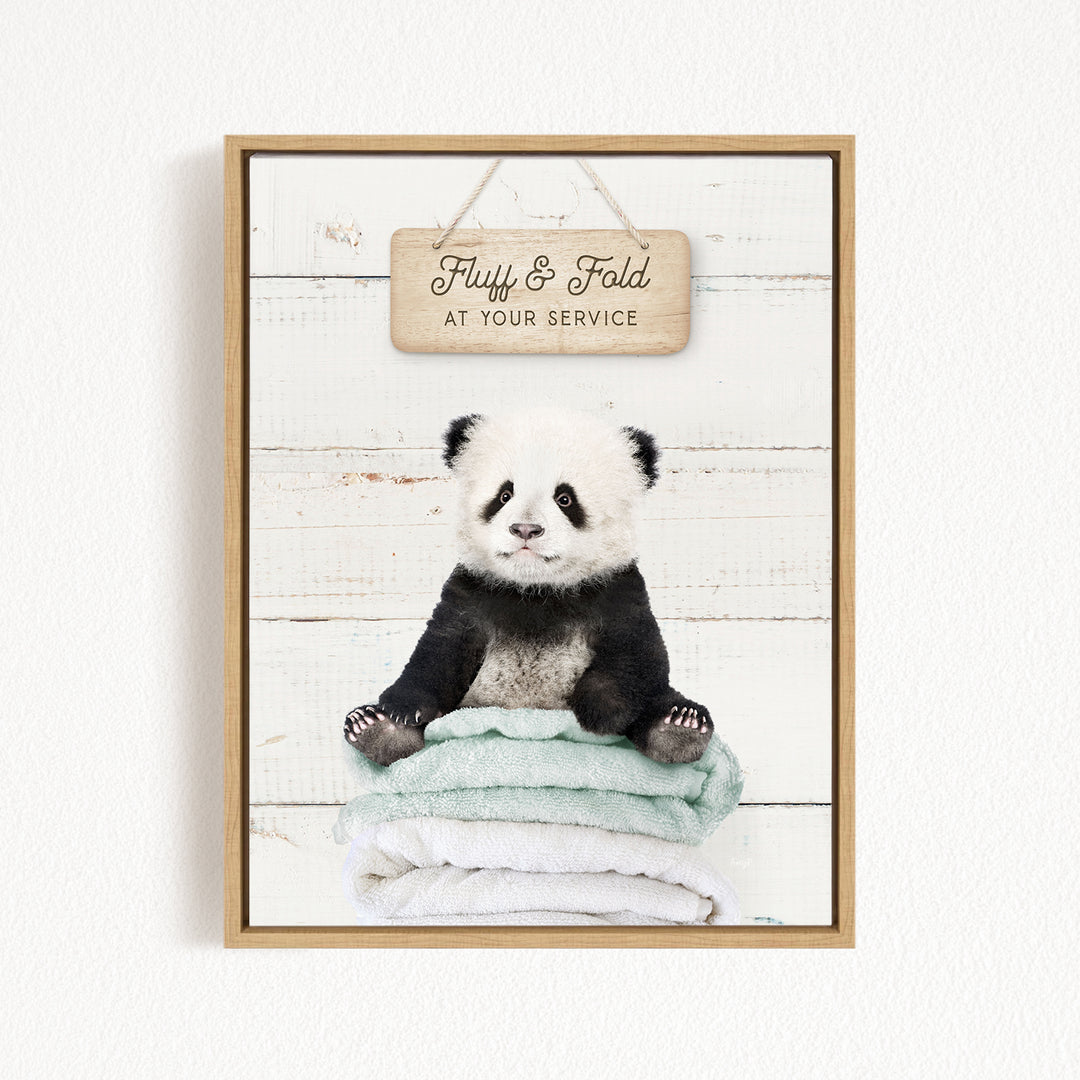 A panda bear sitting on a stack of towels, with a wooden sign above that says "Fluffy & Fold at your Service".