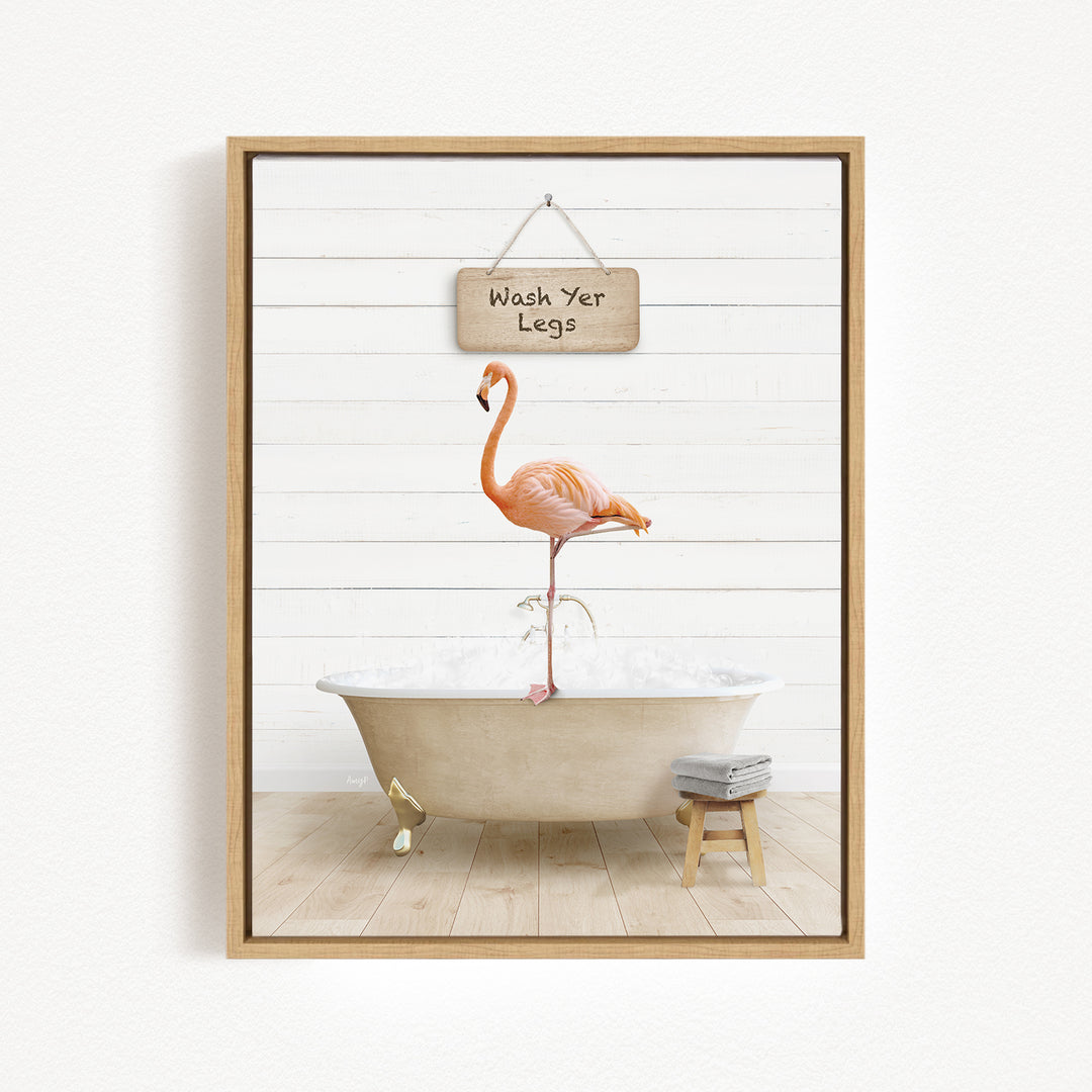 A framed image depicting a pink flamingo standing on a white bathtub, with a sign above it that reads "Wash Your Legs".