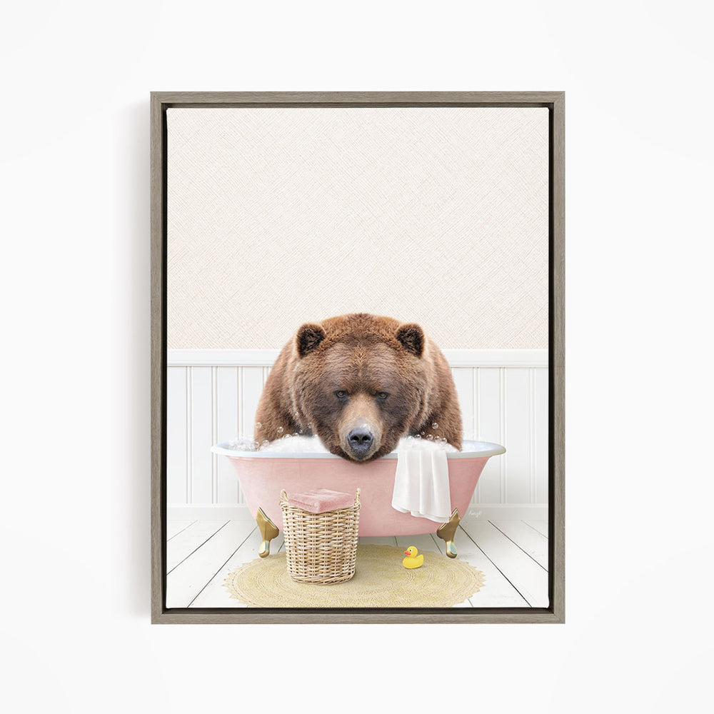 A brown bear is sitting in a pink bathtub, surrounded by a yellow rubber duck and a white towel.