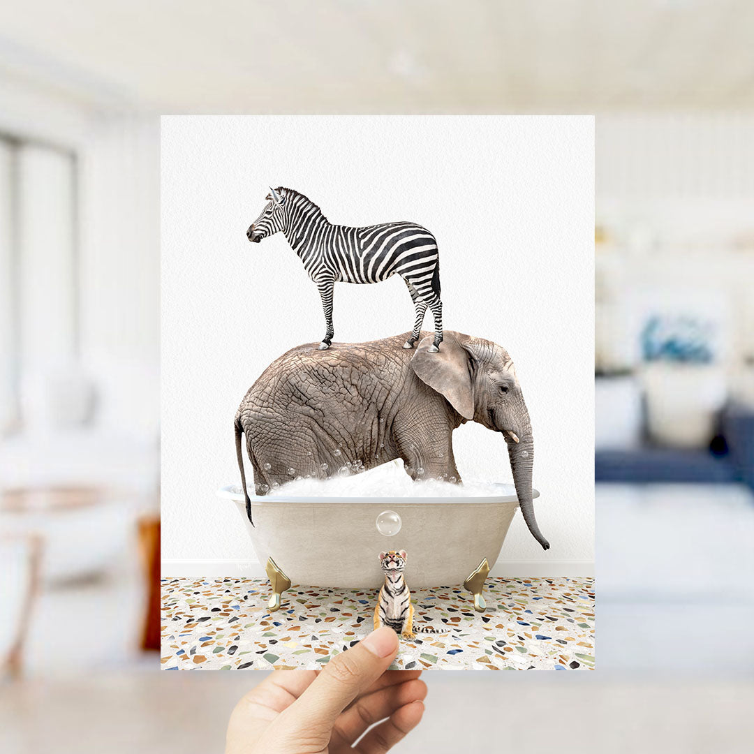 A hand holds up a collage of two images: a zebra standing on an elephant's back in a bathtub, and a small elephant standing in a bathtub with a bubble.