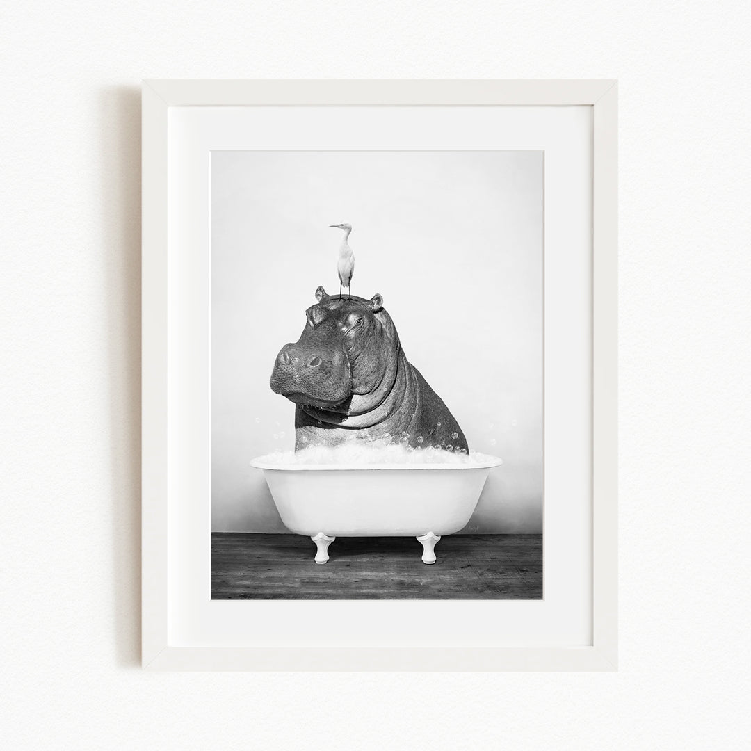 A black and white photograph of a hippopotamus sitting in a bathtub, with a bird perched on its head.
