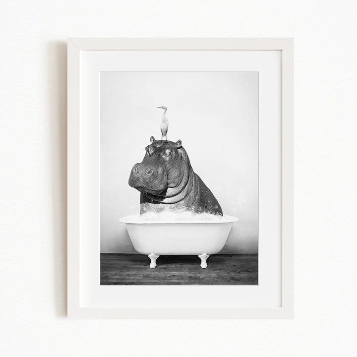A black and white photograph of a hippopotamus sitting in a bathtub, with a bird perched on its head.