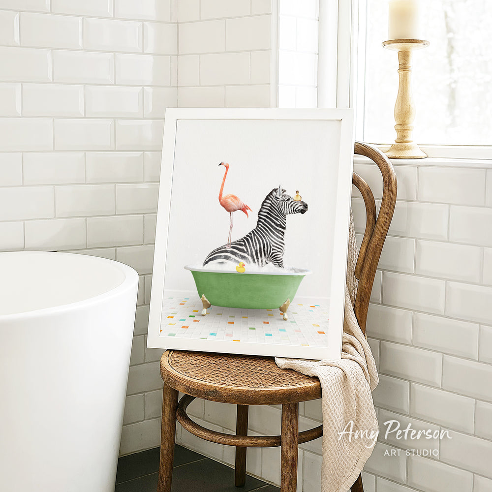A framed image of a zebra sitting in a green bathtub, with a pink flamingo standing on its back, is displayed on a wooden chair in a bathroom setting.