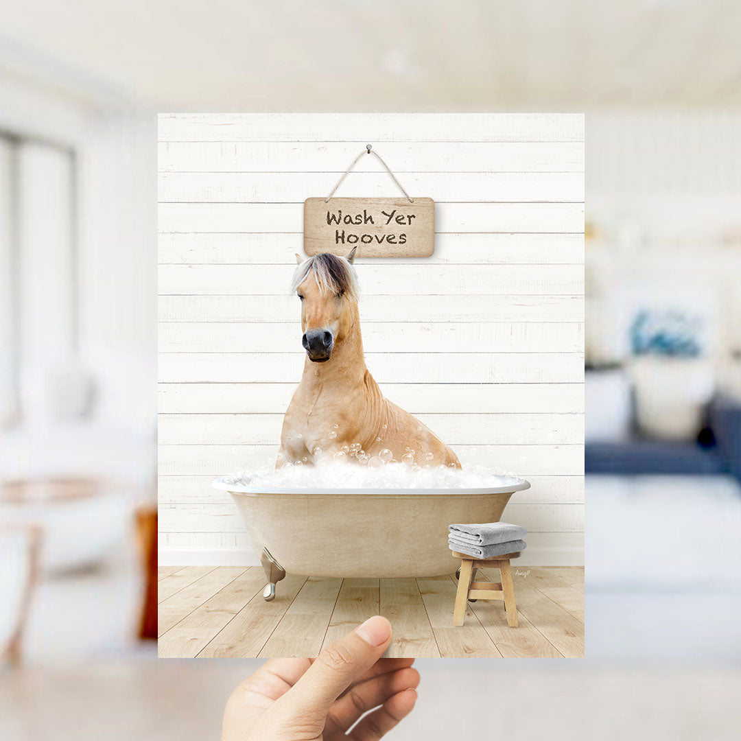 A hand holds up a framed image of a horse sitting in a bathtub, with a sign above it that says "Wash Yer Hooves".