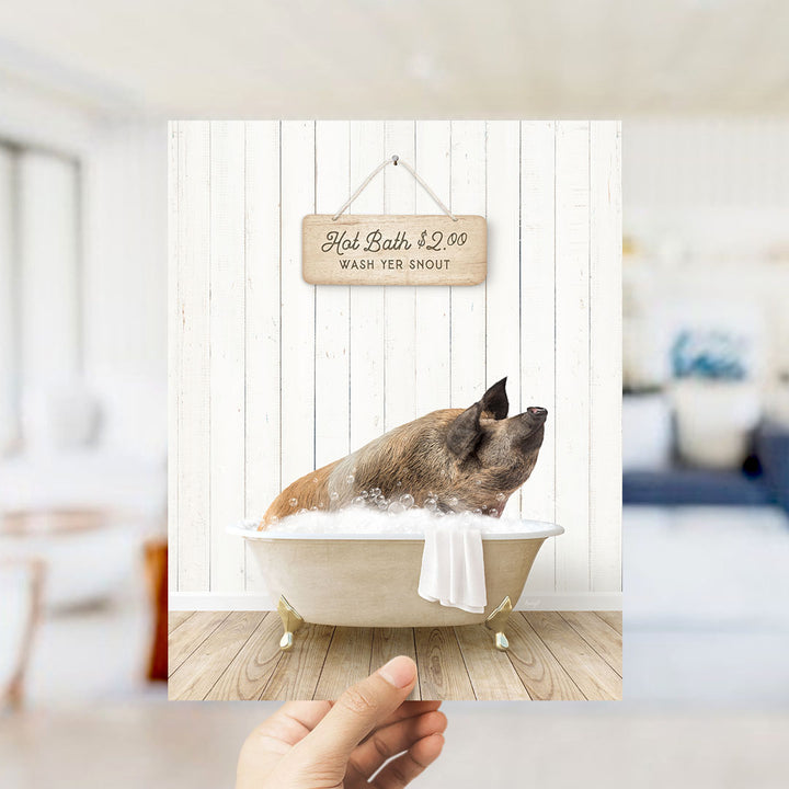 A hand holding a framed image of a pig sitting in a bathtub, with a sign above it advertising hot baths for $2.00.