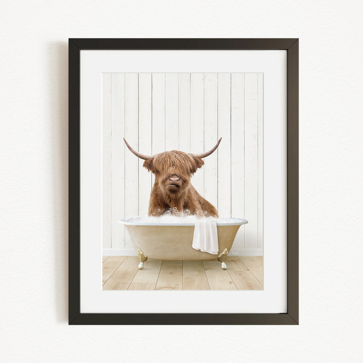A brown Highland cow with large horns is sitting in a white bathtub, with a towel draped over the side of the tub.