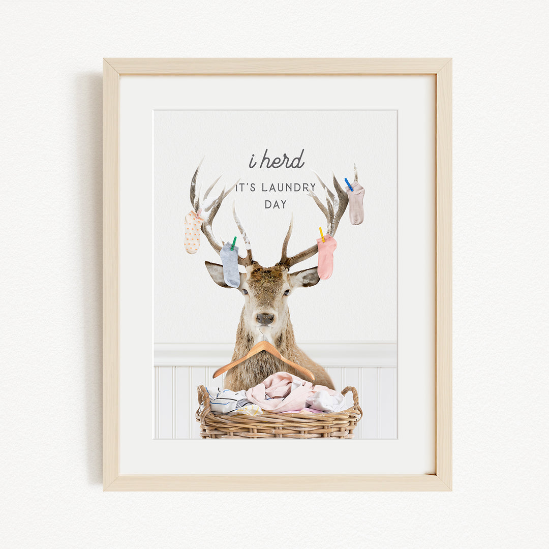A framed image depicting a deer with antlers holding laundry, accompanied by the text "I herd it's laundry day".