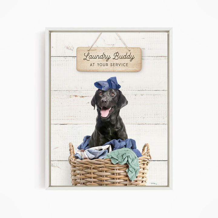 A black dog wearing a blue hat sits in a wicker laundry basket, with a wooden sign above that reads "Laundry Buddy at your service".