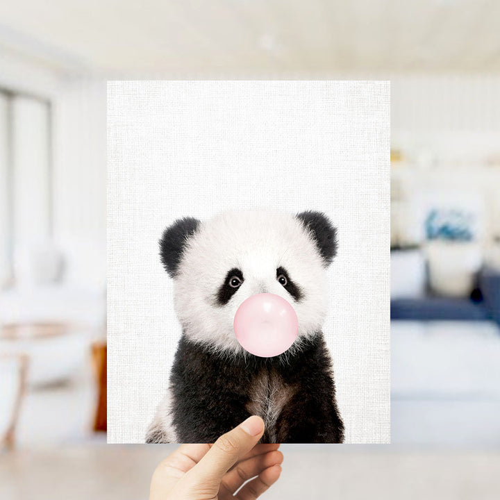 A hand is holding up a framed image of a panda bear blowing a bubble with a pink bubble gum bubble.