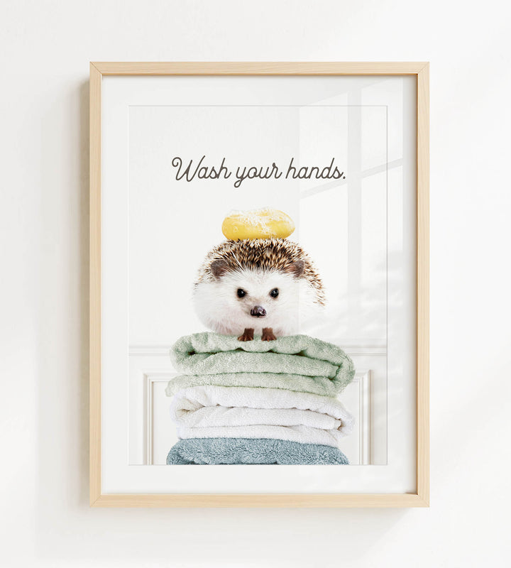 A framed image of a hedgehog sitting atop a stack of towels, with the text "Wash your hands" written above it.