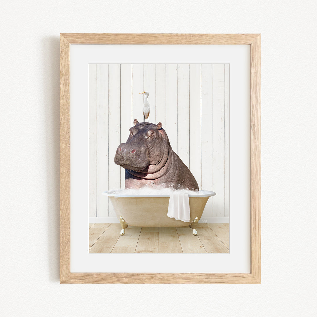 A framed image depicting a hippopotamus sitting in a bathtub, with a bird perched on its head.