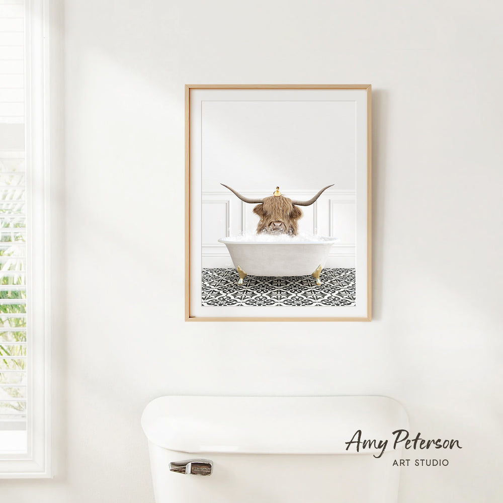 A framed image of a Highland cow sitting in a bathtub, with a patterned tile floor beneath it.