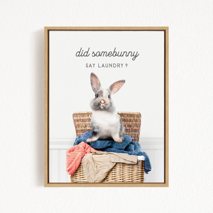 A gray and white rabbit sitting in a wicker basket filled with laundry, with the text "did some bunny say laundry?" displayed above the image.