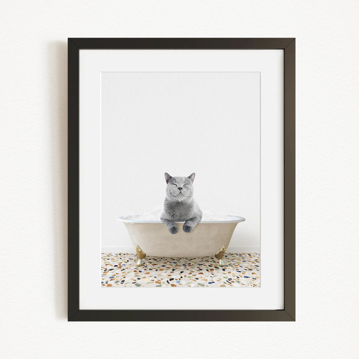 A gray cat sitting in a white bathtub filled with bubbles, with a mosaic floor in the background.