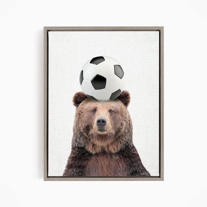 A brown bear balancing a soccer ball on its head.