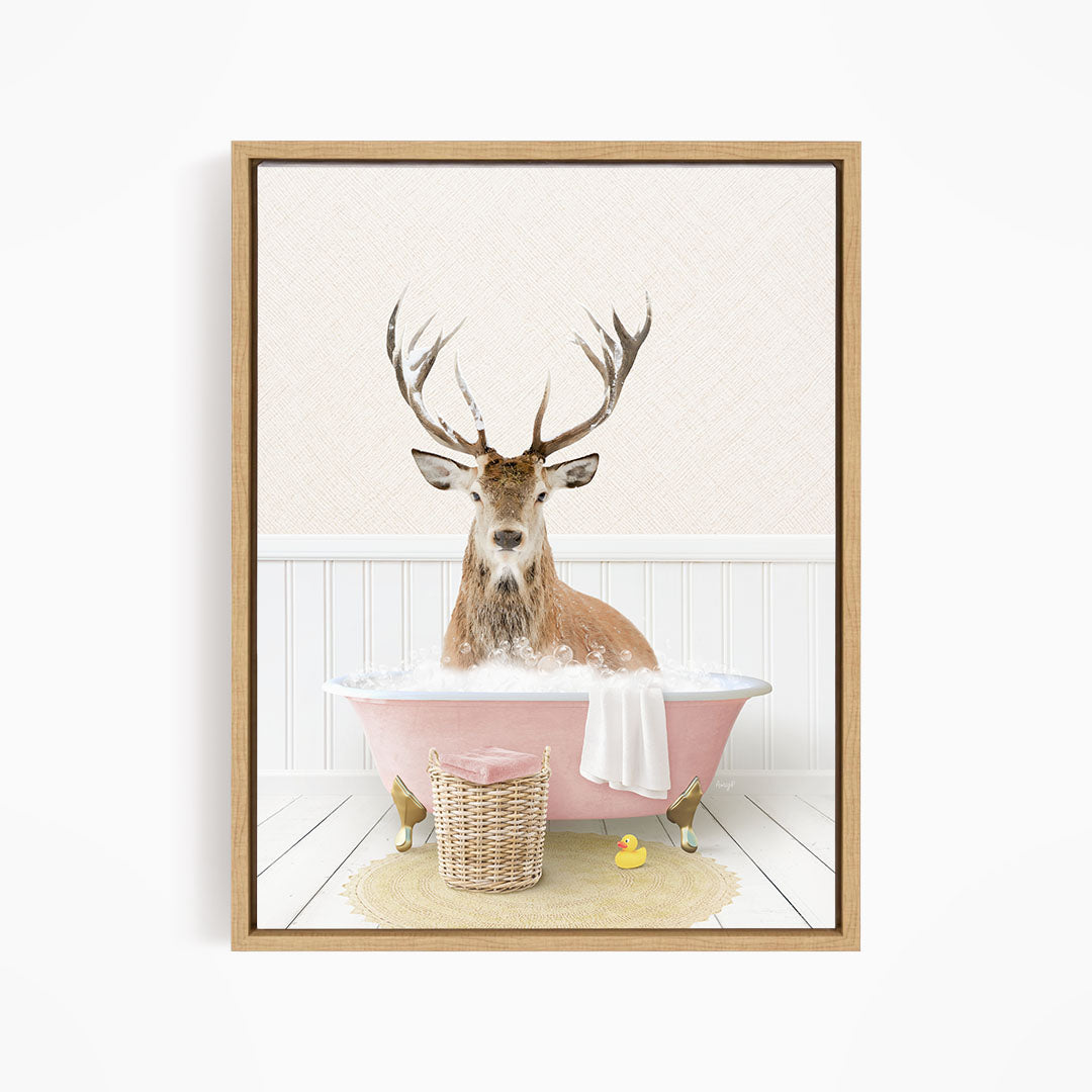 A deer with antlers is sitting in a pink bathtub filled with bubbles, surrounded by a yellow rubber duck and a basket.