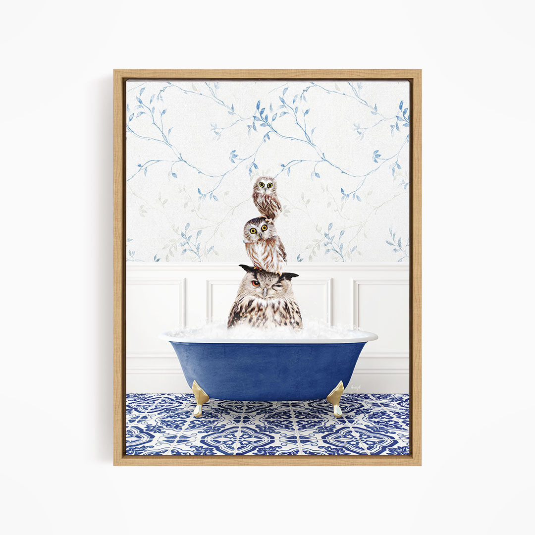 A framed image depicting a group of owls sitting in a blue bathtub, with a patterned tile floor and a floral wallpaper in the background.