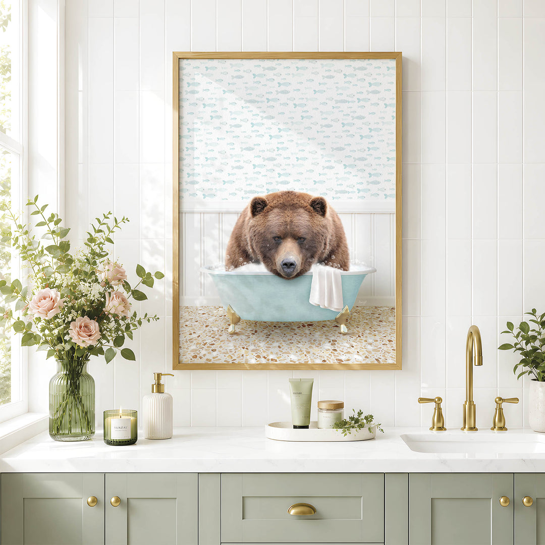 A framed image of a brown bear sitting in a bathtub, surrounded by flowers and a green vase, with a white sink and gold fixtures in the background.