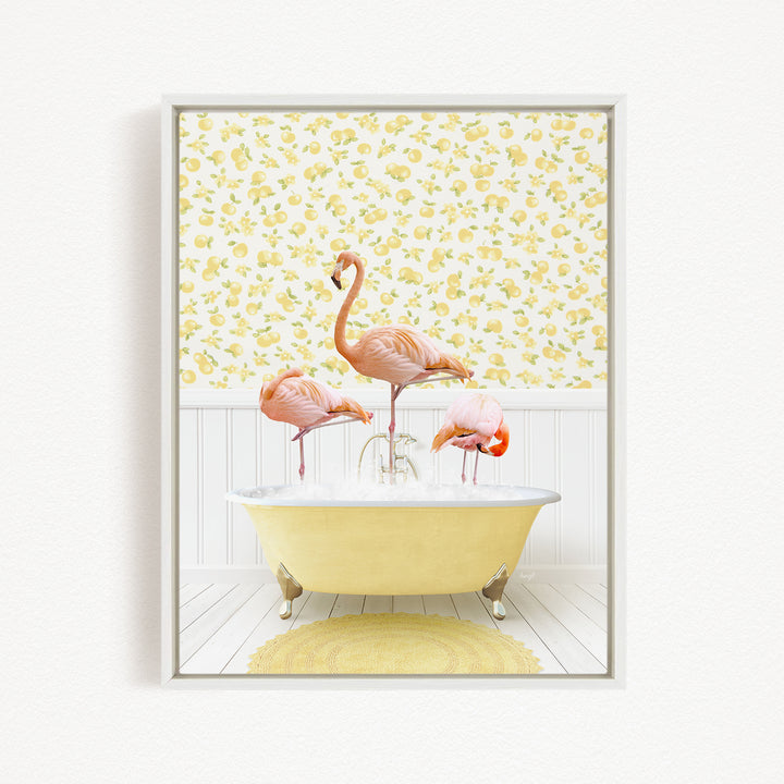 A framed image depicting three pink flamingos standing in a yellow bathtub, with a yellow and white floral wallpaper in the background.