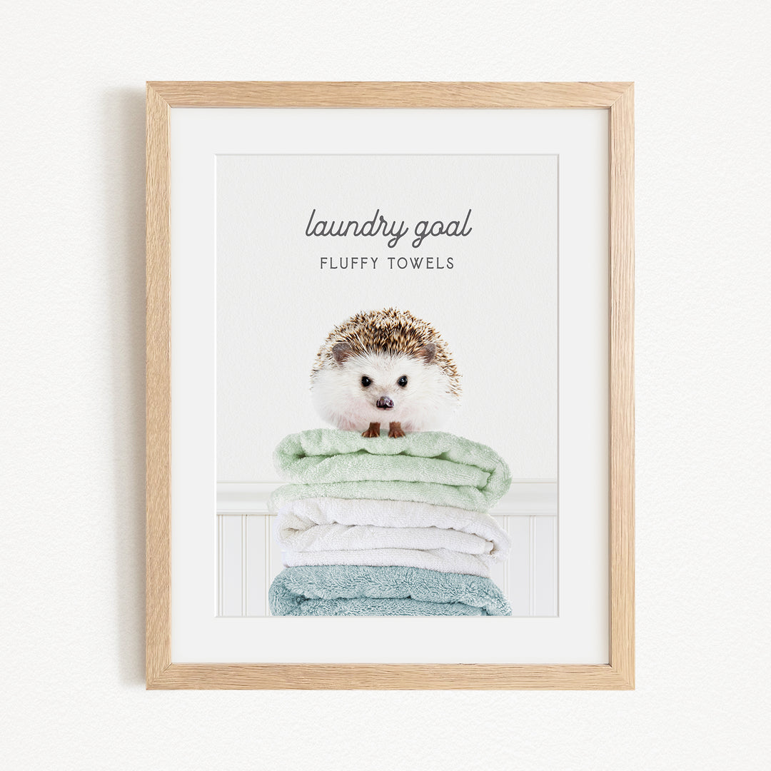 A framed image of a hedgehog sitting atop a stack of fluffy towels, with the text "laundry goal" and "fluffy towels" written above it.
