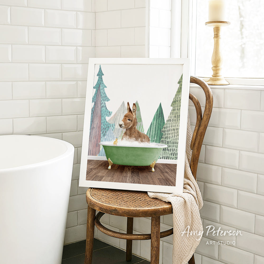 A framed painting of a rabbit sitting in a green bathtub, surrounded by trees, is displayed on a wooden chair in a bathroom setting.