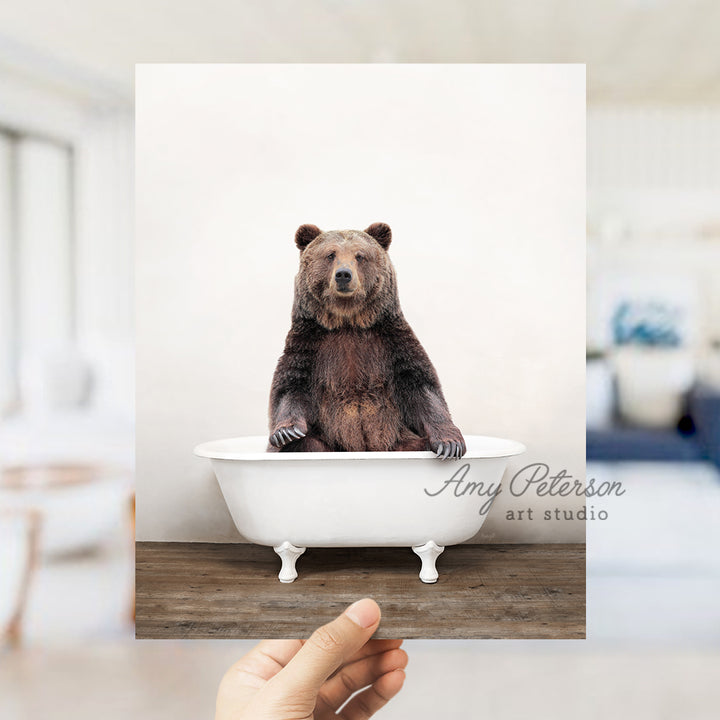 a hand holding a polaroid of a bear in a bathtub