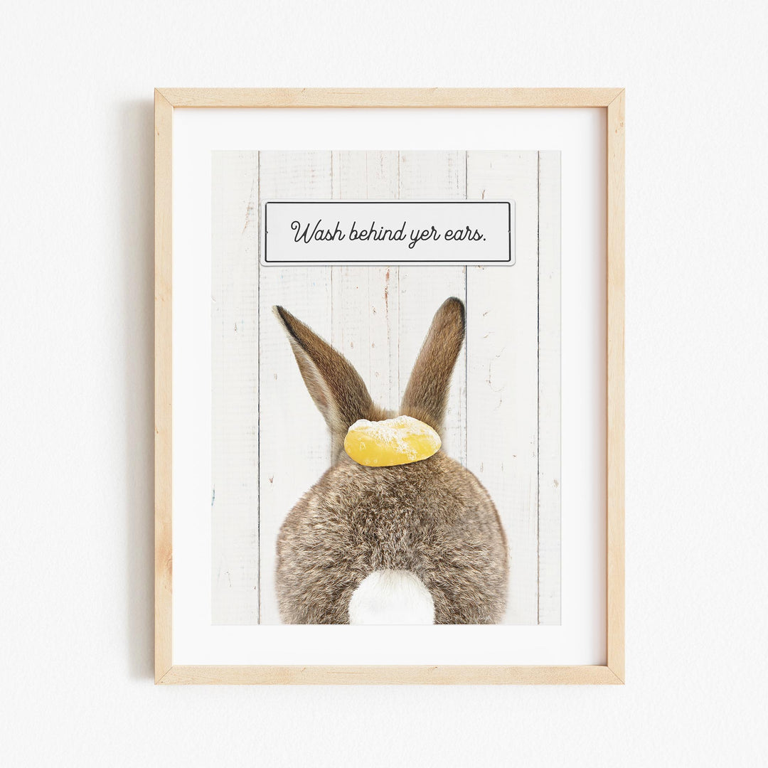 A framed image of a rabbit with a yellow object on its back, accompanied by the text "Wash behind your ears."