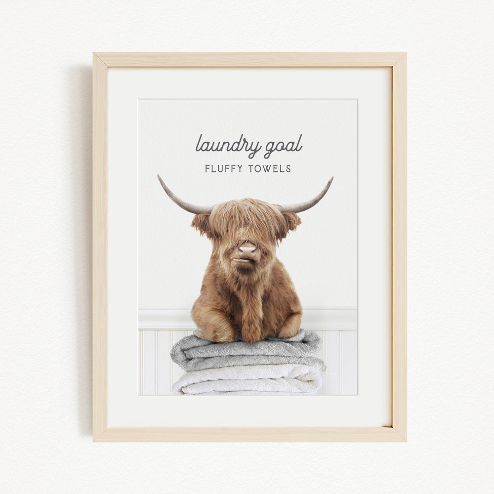 A framed image of a brown, shaggy-haired animal with large horns, sitting on a stack of fluffy towels.