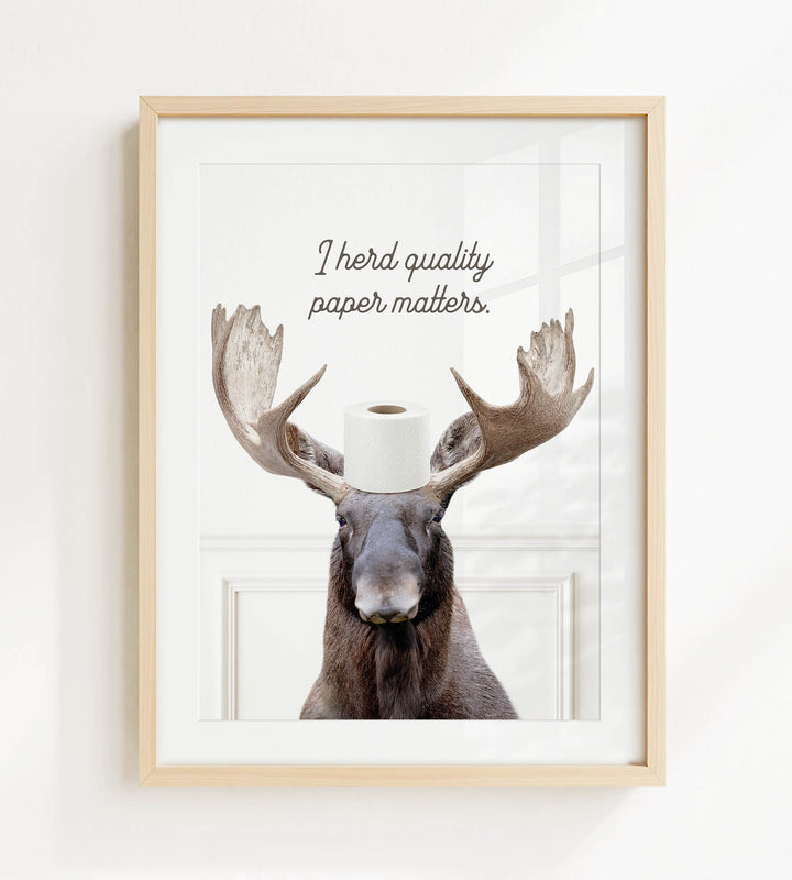 A framed image of a moose with a roll of toilet paper on its head, accompanied by the text "I herd quality paper matters."