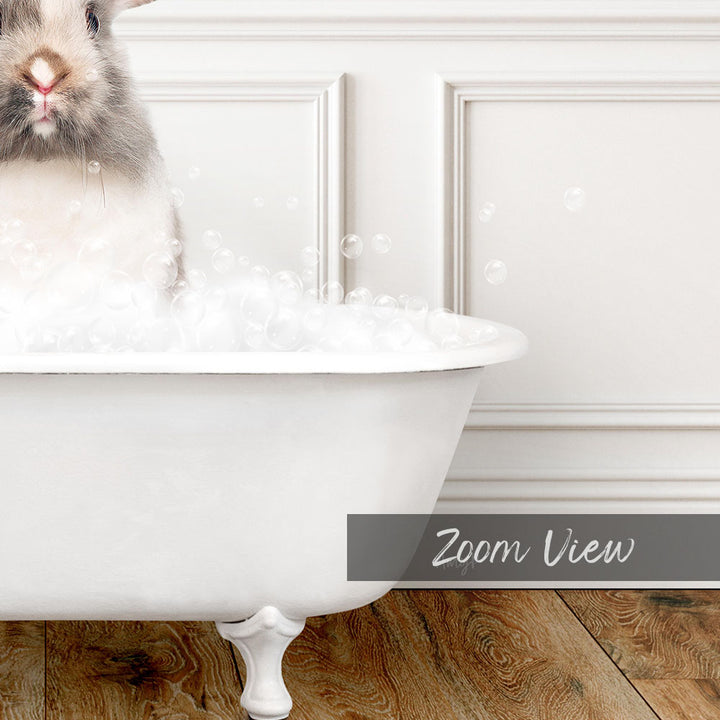A fluffy white rabbit sitting in a white bathtub filled with bubbles, with a wooden floor visible in the background.