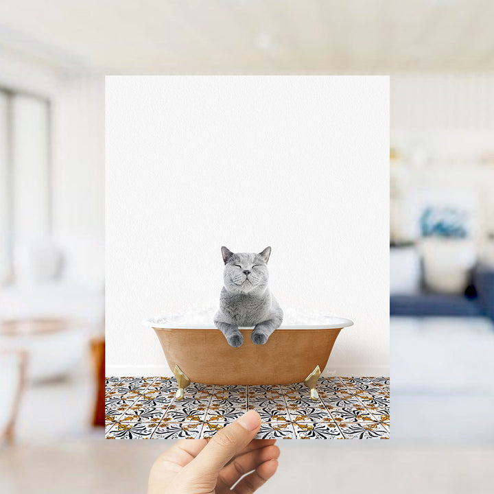 A gray cat sitting in a bathtub filled with bubbles, with a hand holding the image up to the camera.