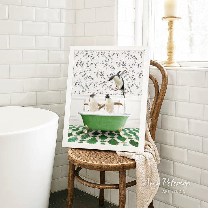 A framed image of penguins sitting in a green bathtub is displayed on a wooden chair in a bathroom setting.