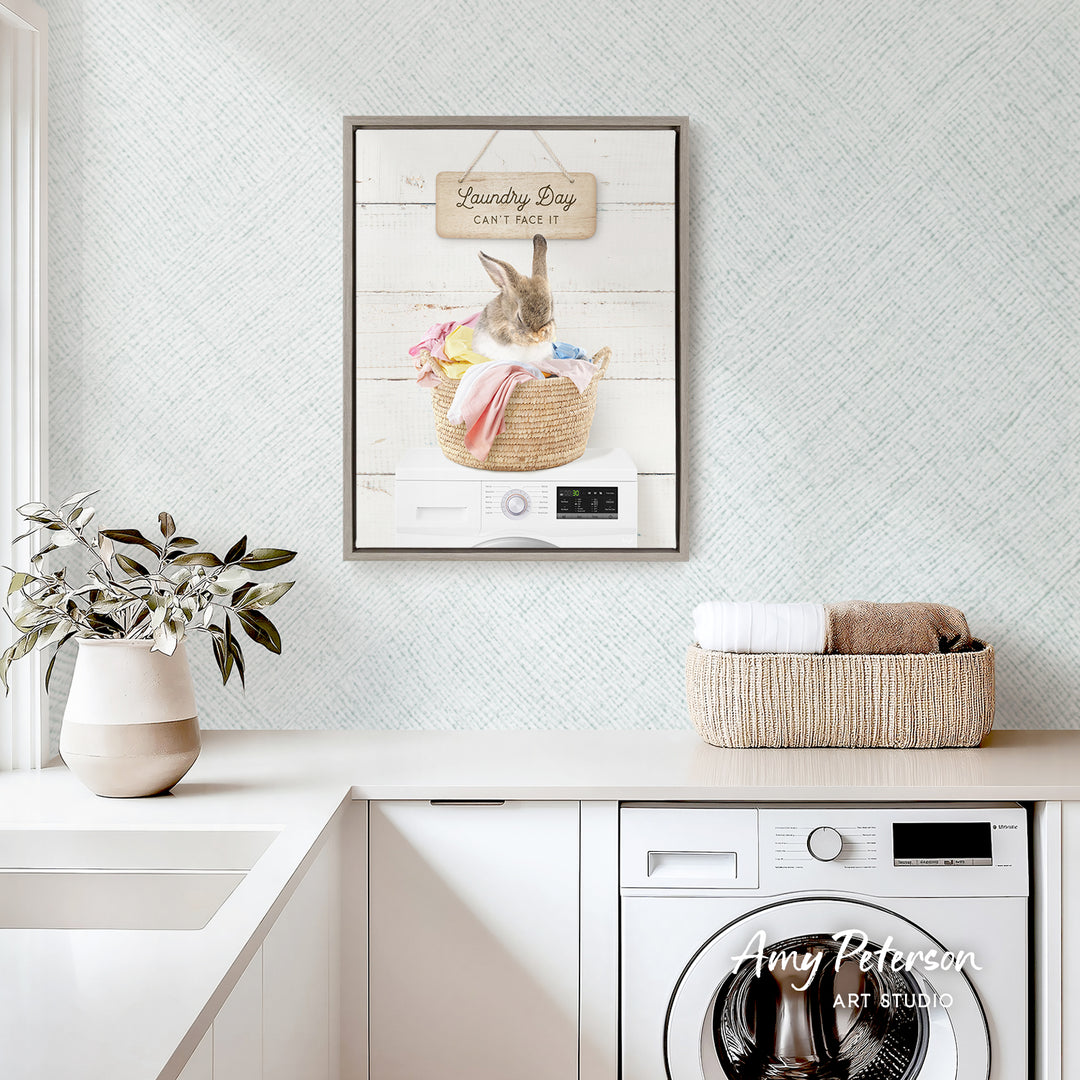 a laundry room with a framed poster of a rabbit sitting in a basket of laundry, a white washing machine, and a potted plant on the counter.