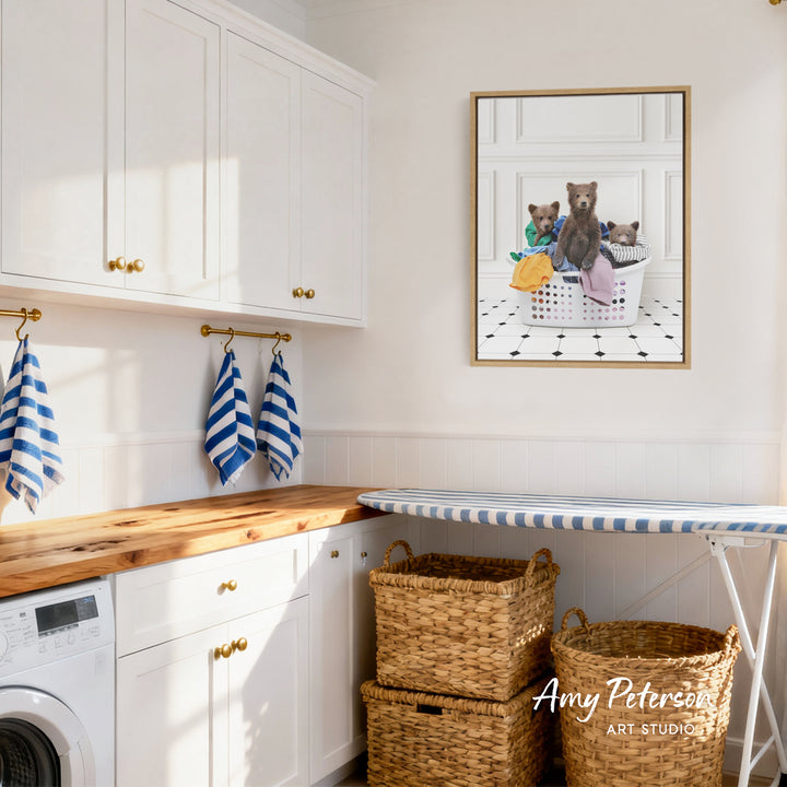 A framed image of three bears sitting in a laundry basket is displayed on the wall in a bright, white-walled room with white cabinets and a wooden countertop.