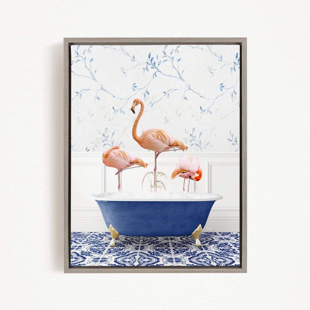 A framed image depicting three flamingos standing in a blue bathtub, with a patterned tile floor and a floral wallpaper in the background.