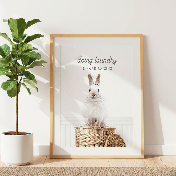 A framed poster with a white rabbit sitting on a woven basket, accompanied by the text "Doing laundry is Hare raising".