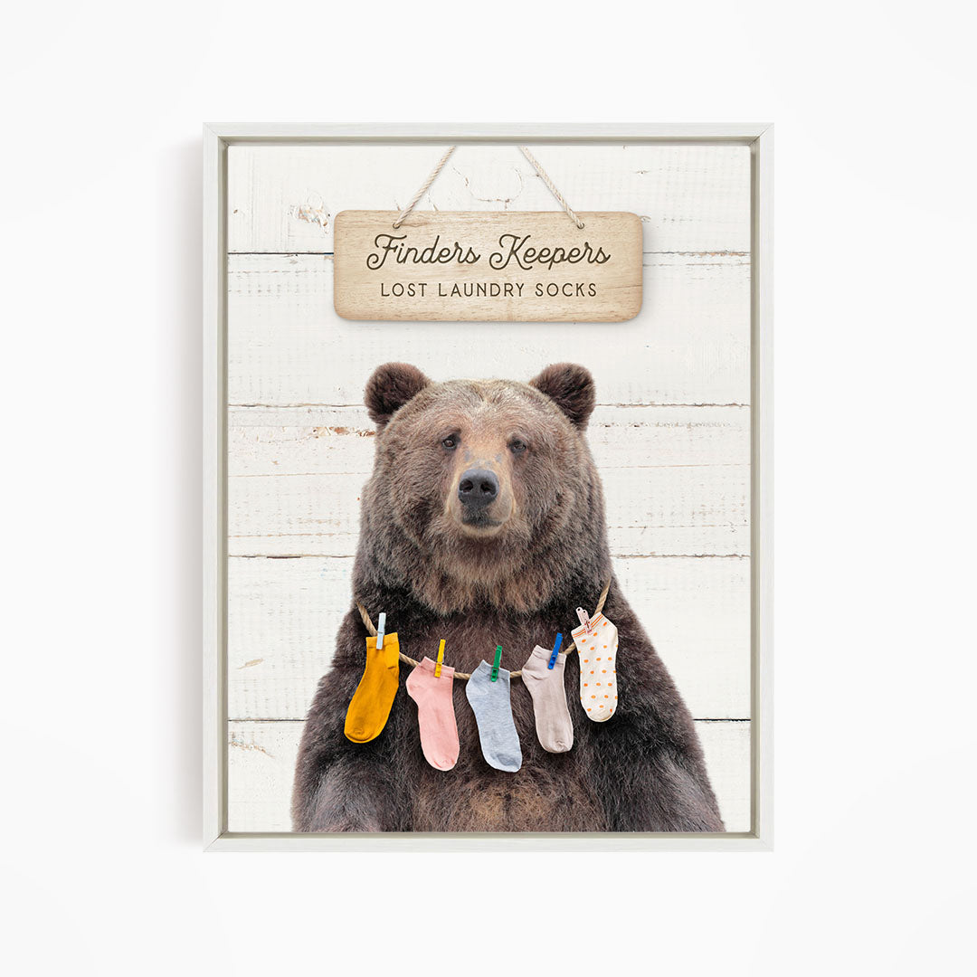 A wooden sign with the text "Finders Keepers" hangs above a bear wearing a pile of colorful socks.