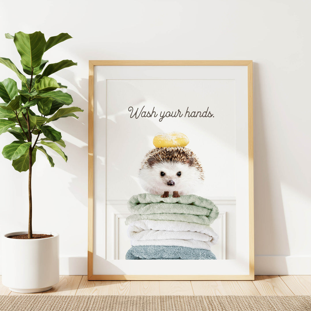 A framed poster with a hedgehog sitting atop a stack of folded towels, accompanied by the text "Wash your hands."