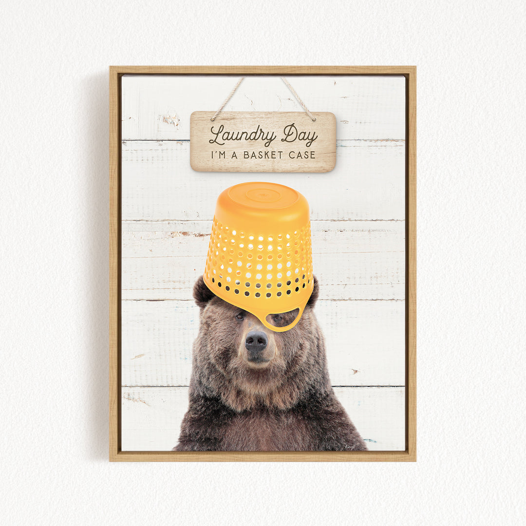 A framed image of a bear wearing a yellow laundry basket on its head, with a wooden sign above that says "Laundry Day I'm a basket case".