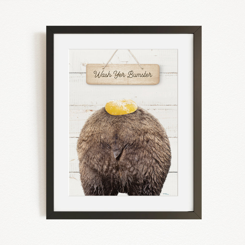 A framed image of a bear with a yellow object on its head, accompanied by a wooden sign that reads "Wash Your Bummer".