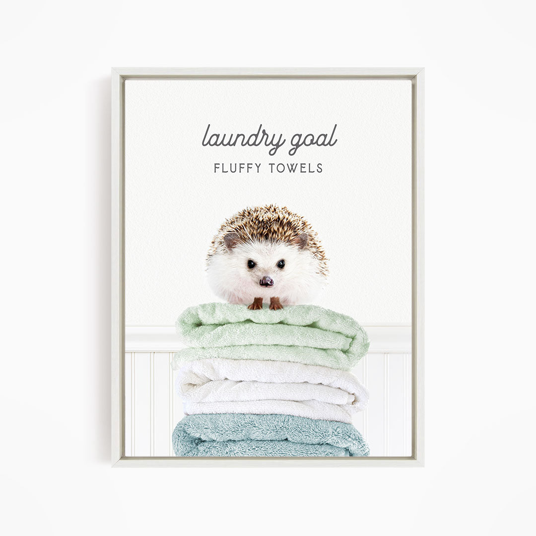 A cute hedgehog sitting atop a stack of fluffy towels, with the text "laundry goal FLUFFY TOWELS" displayed above it.