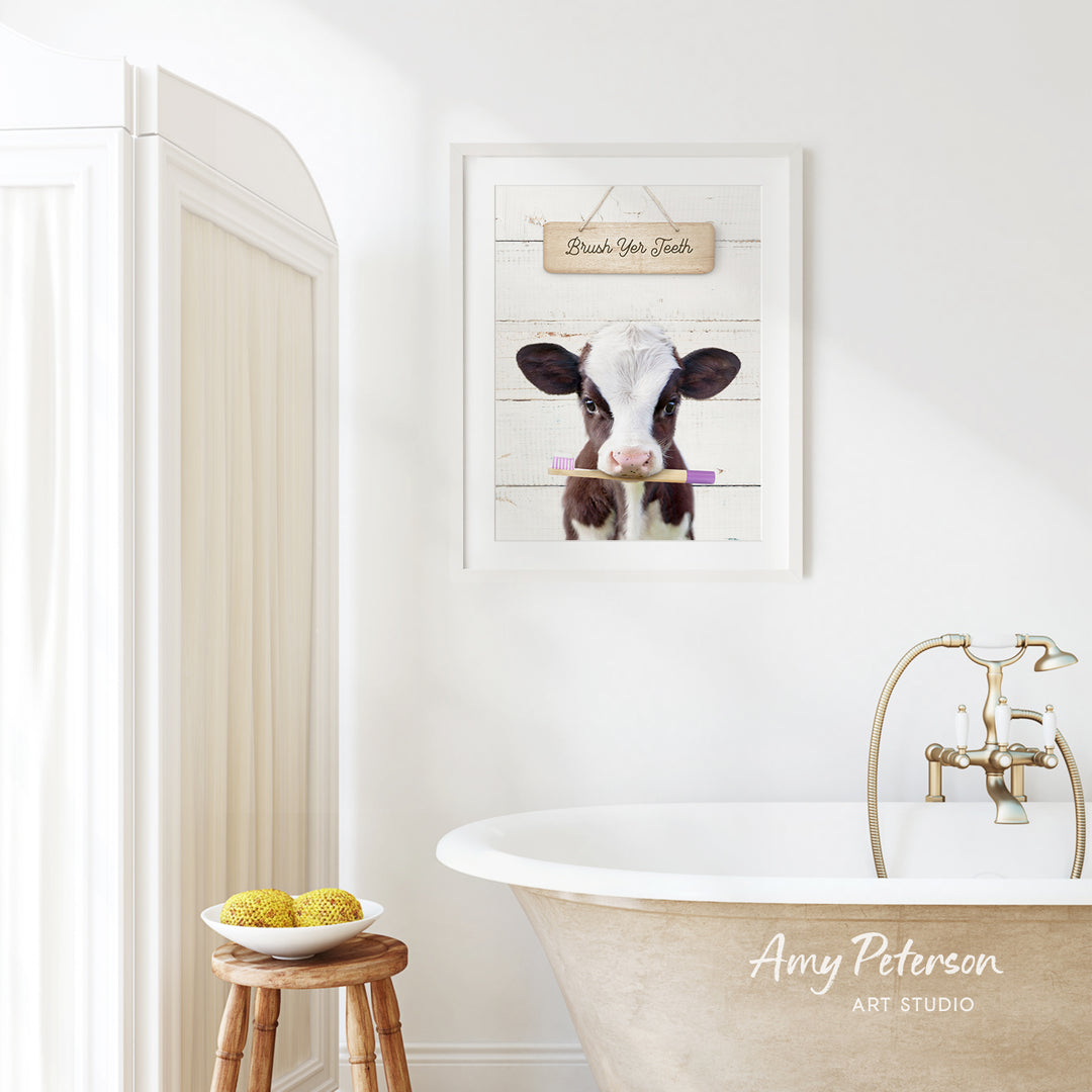a bathroom with a white bathtub, a wooden stool, and a framed picture of a cow holding a toothbrush.