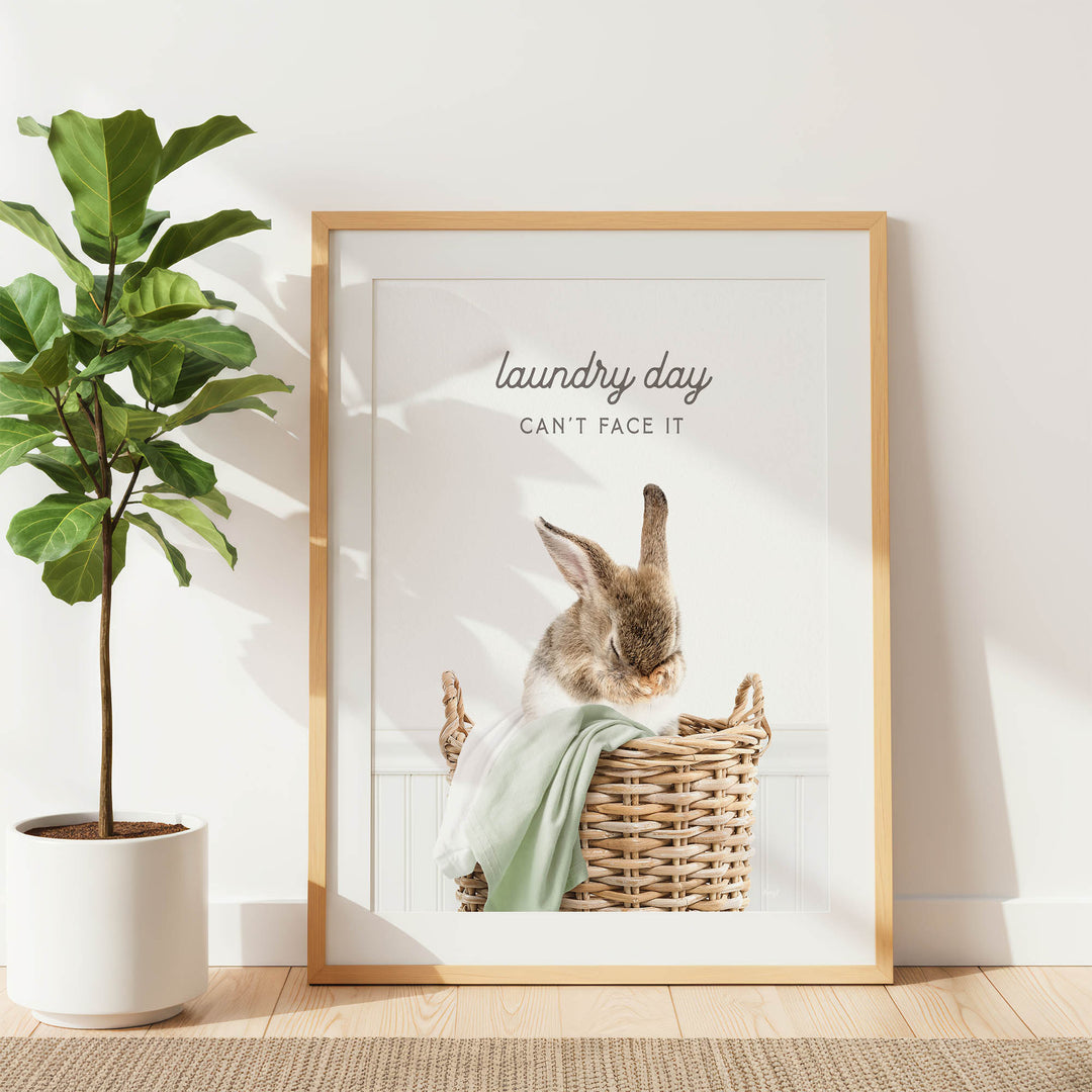A framed image of a rabbit sitting in a wicker basket, with the text "laundry day can't face it" written above the rabbit.
